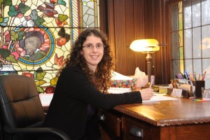 A woman sitting at a desk in front of stained glass.